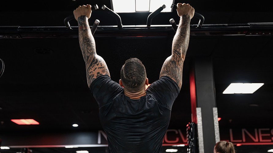 En mand der udf�rer pull-ups ses bagfra, i et tr�ningsmilj�.